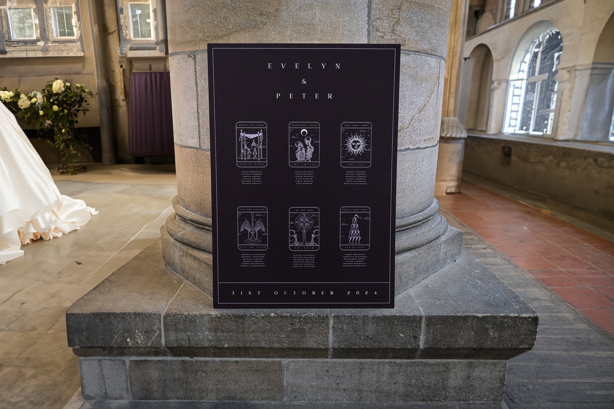 Luxury gothic wedding seating chart with vintage tarot card design, dramatic dark palette, set against a stone church pillar.