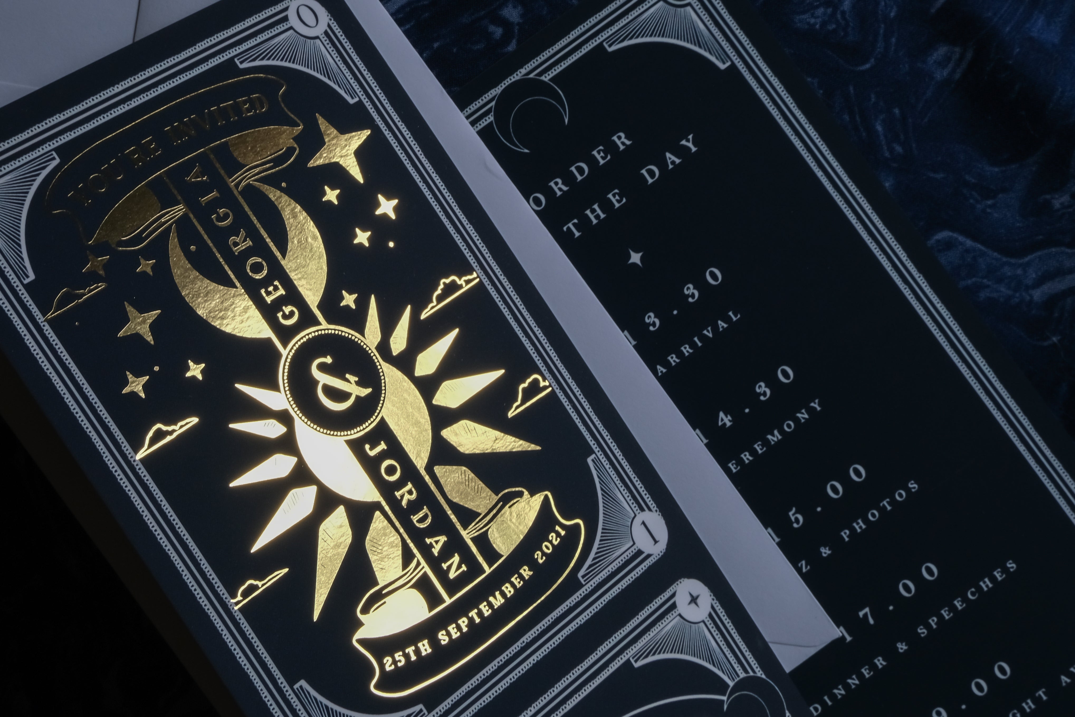 Close-up of a luxury UK celestial wedding stationery suite with gold foil, moon and star motifs, and a schedule card beside RSVP.