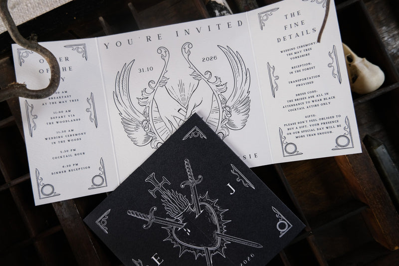 Luxury gatefold wedding invitation suite with black and white gothic design, sword and wing art, dramatic motifs, and elegant text.