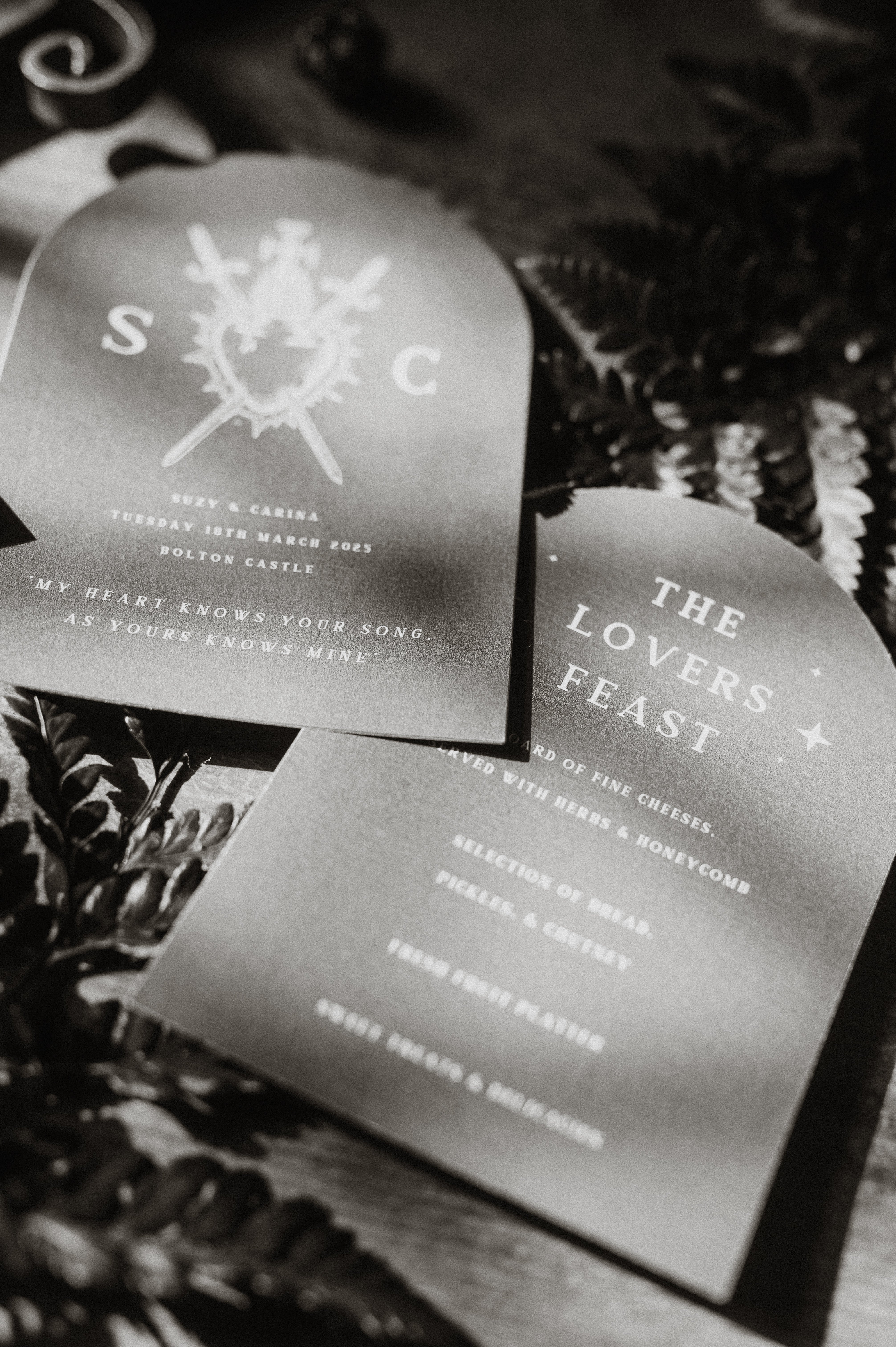 Luxury arched wedding menus with vintage-inspired design rest on a table, accented by ferns and romantic, warm lighting.