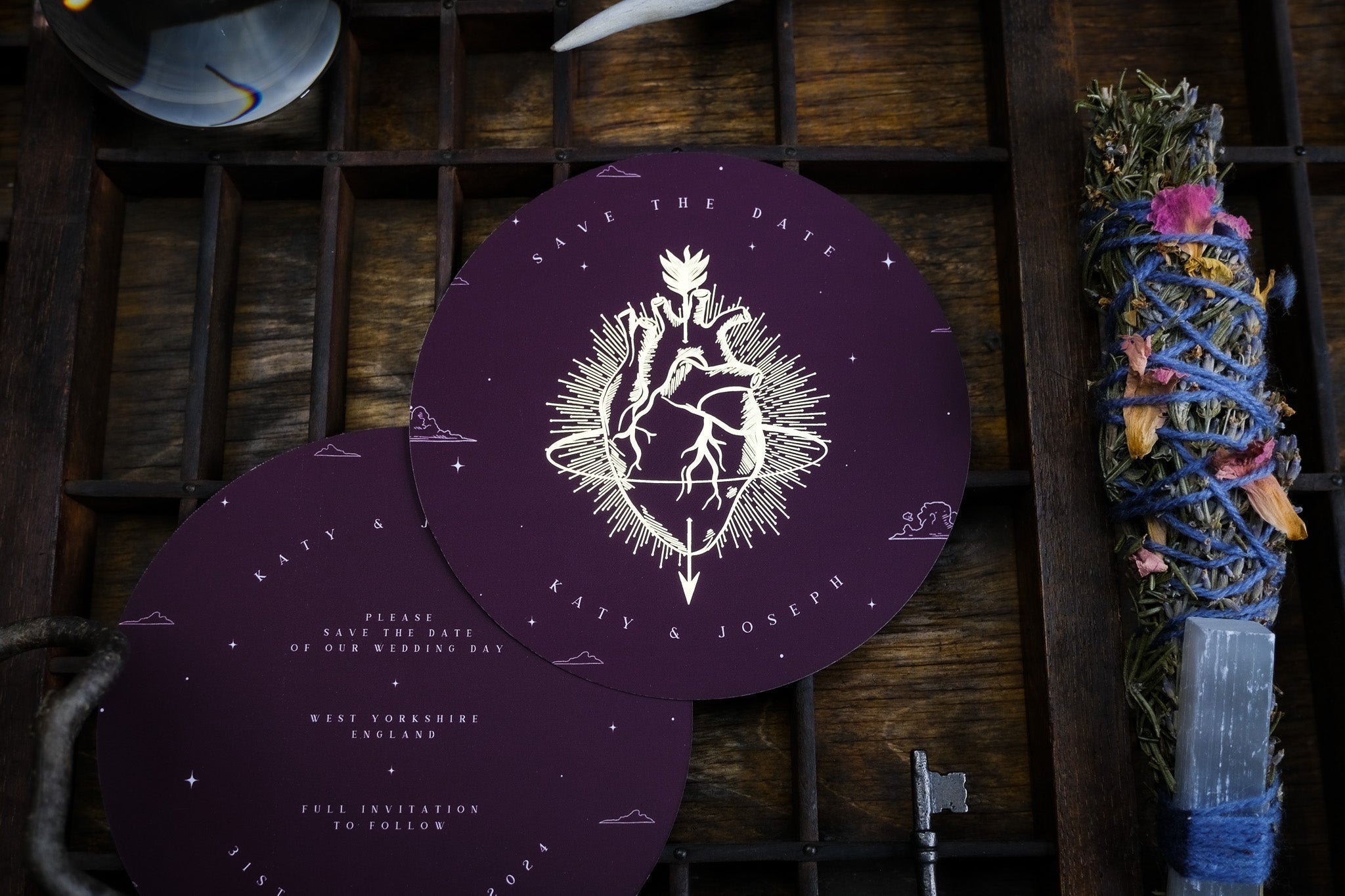 Luxury circular wedding save the date cards with gold foil anatomical heart on deep purple, styled with dried herbs and a vintage key.