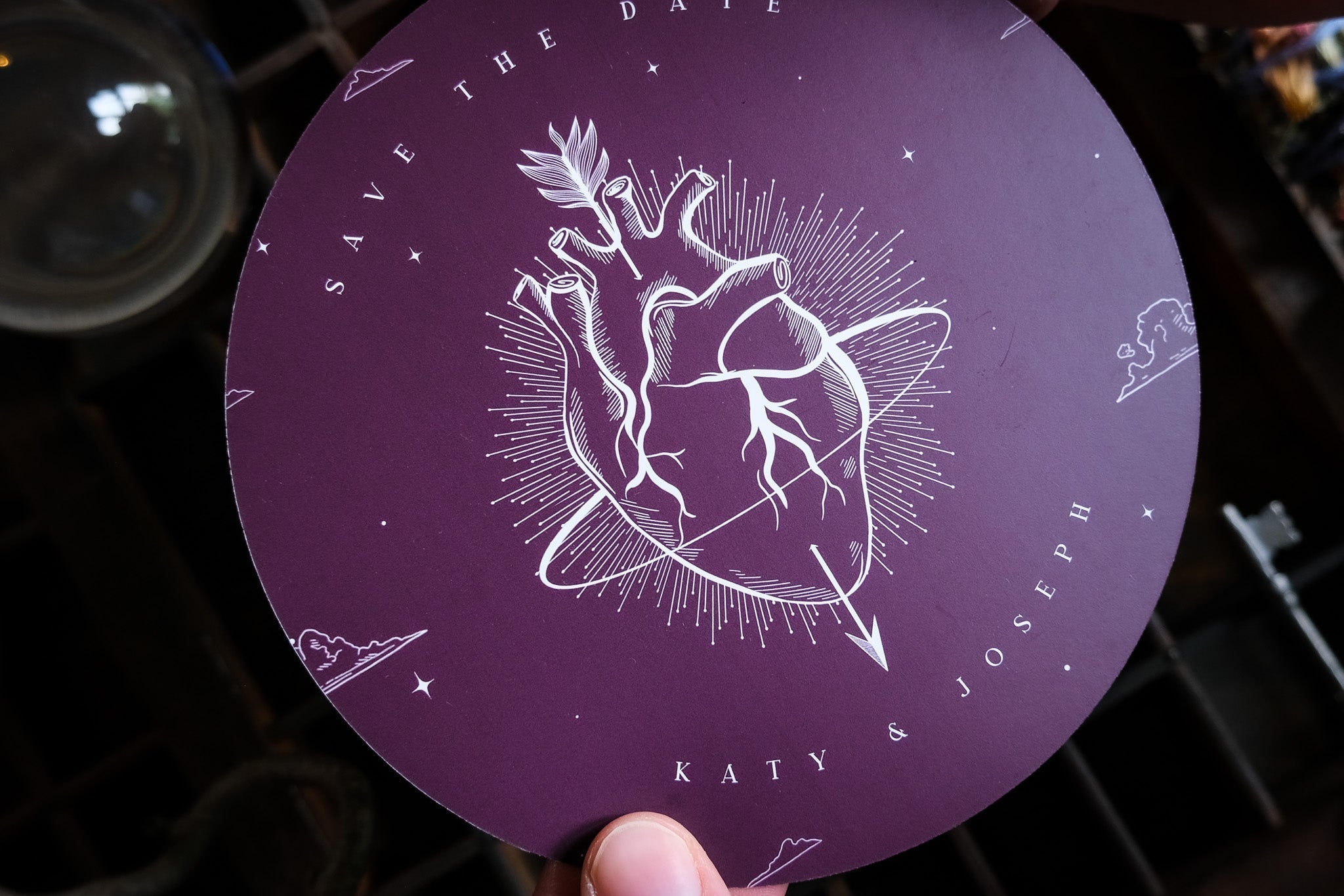 Luxury circular purple Save the Date card in a gothic style, with white anatomical heart, radiant rays, and cloud motifs; wedding stationery UK.
