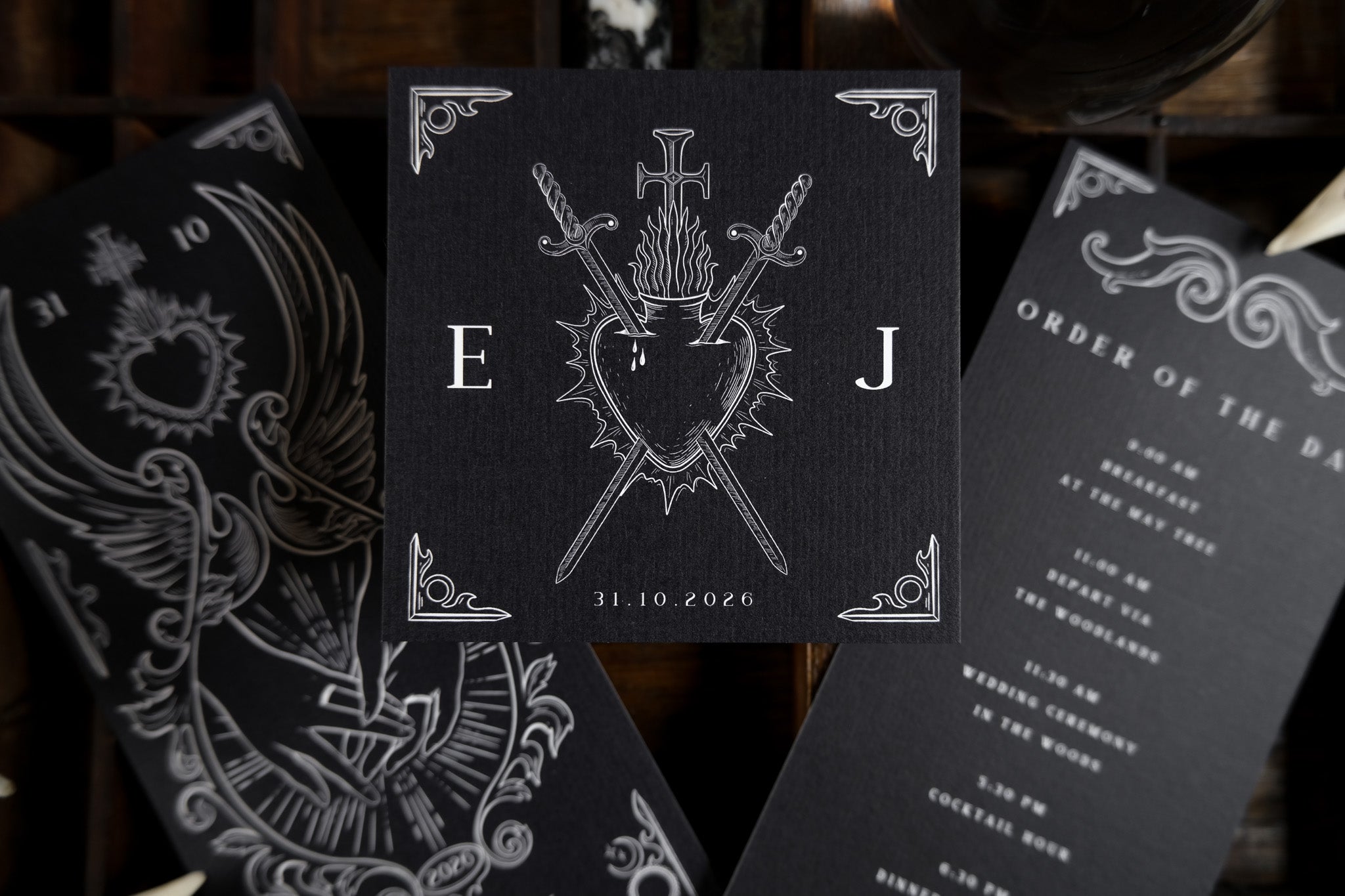 Luxury gothic wedding stationery suite with dramatic black cards, ornate white sword and heart motif, and vintage-inspired detailing.