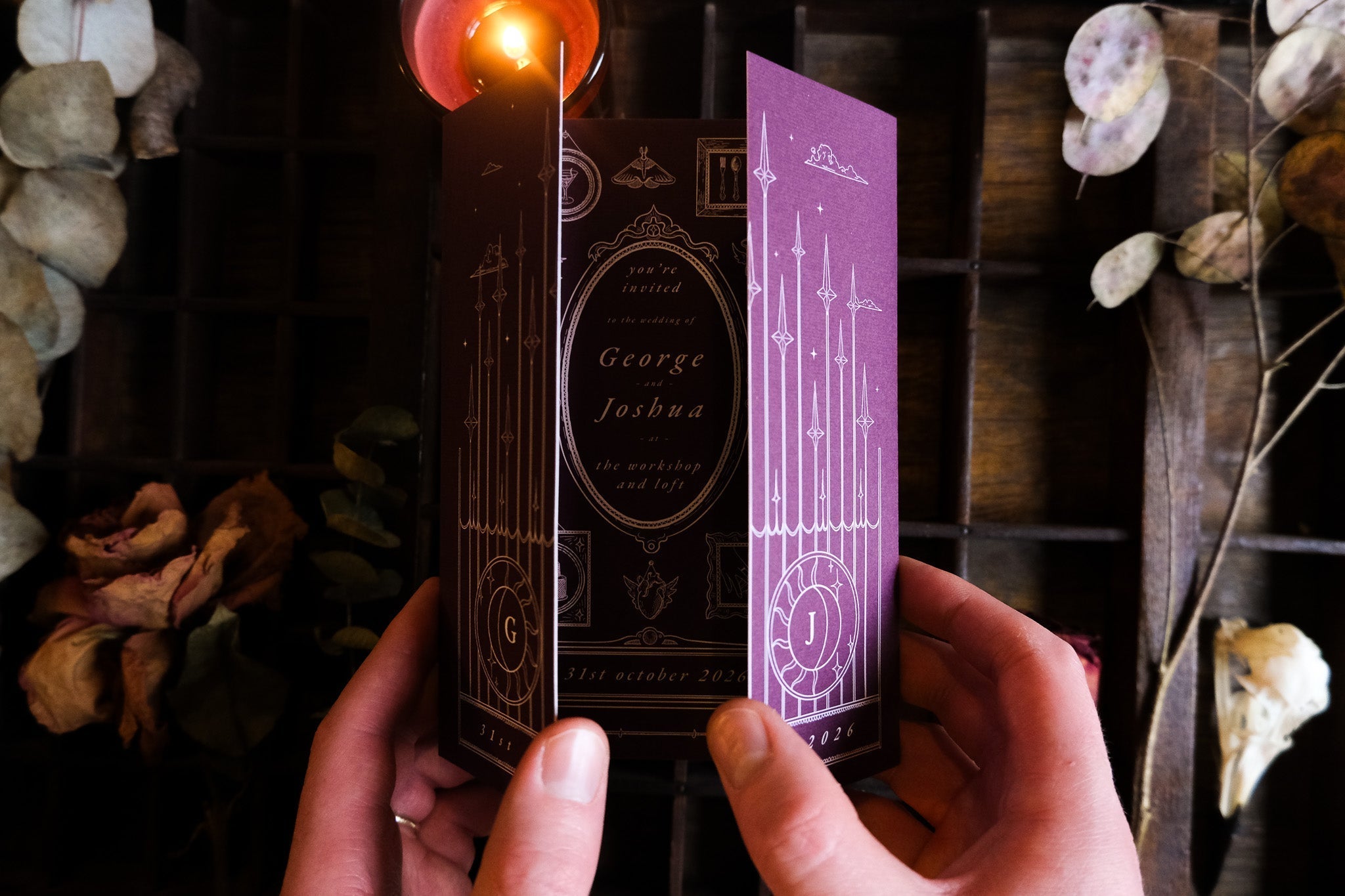 A gatefold wedding invitation in deep purple with gothic candle motifs, luxury cardstock; styled with a lit candle and dried flowers.
