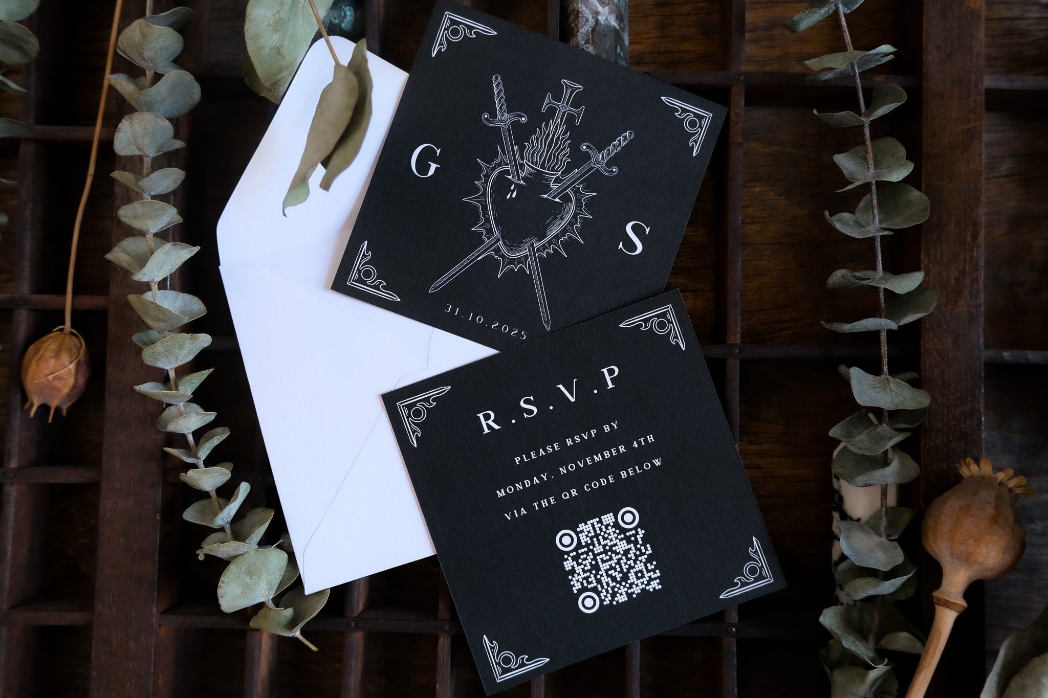 Luxury gothic wedding stationery set featuring a dramatic black RSVP card with white mystical design, QR code, and white envelope on wood.