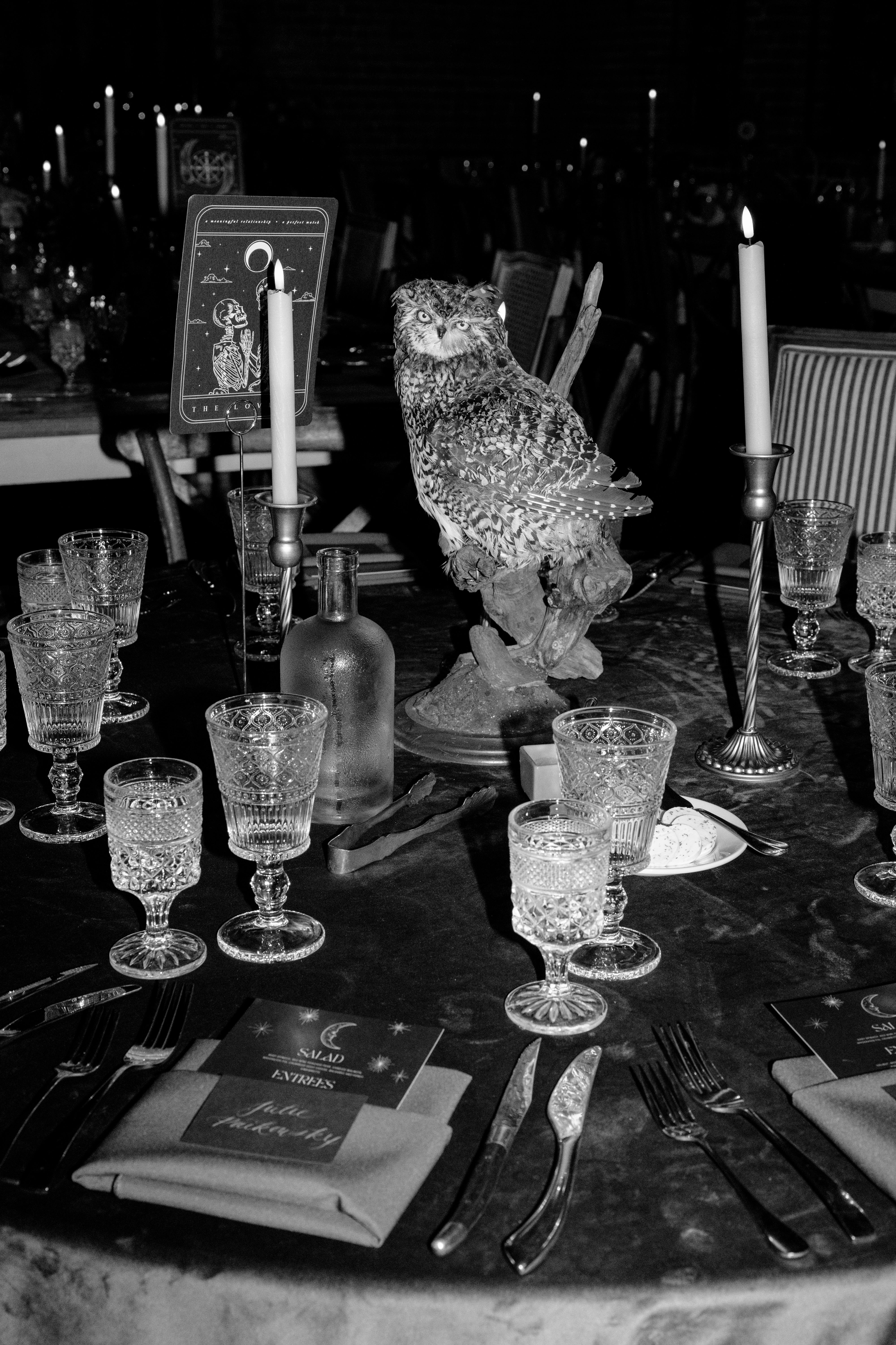 A vintage formal UK dinner table with luxury black-and-white personalised wedding stationery, crystal glassware, and a gothic owl centerpiece.