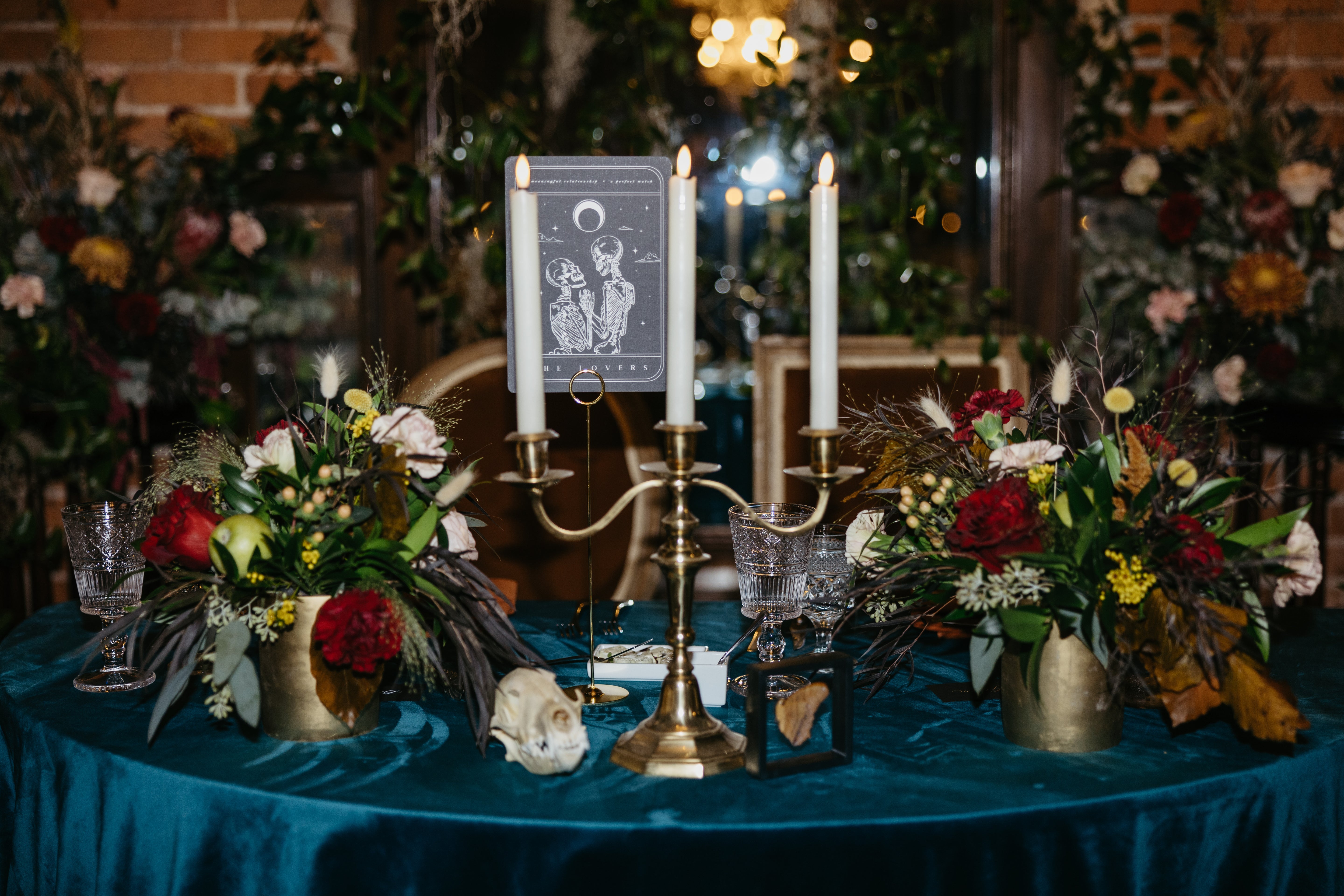 Luxury UK wedding stationery displayed on a dramatic gothic table with green velvet, tarot accents, brass candelabra, and lush florals.