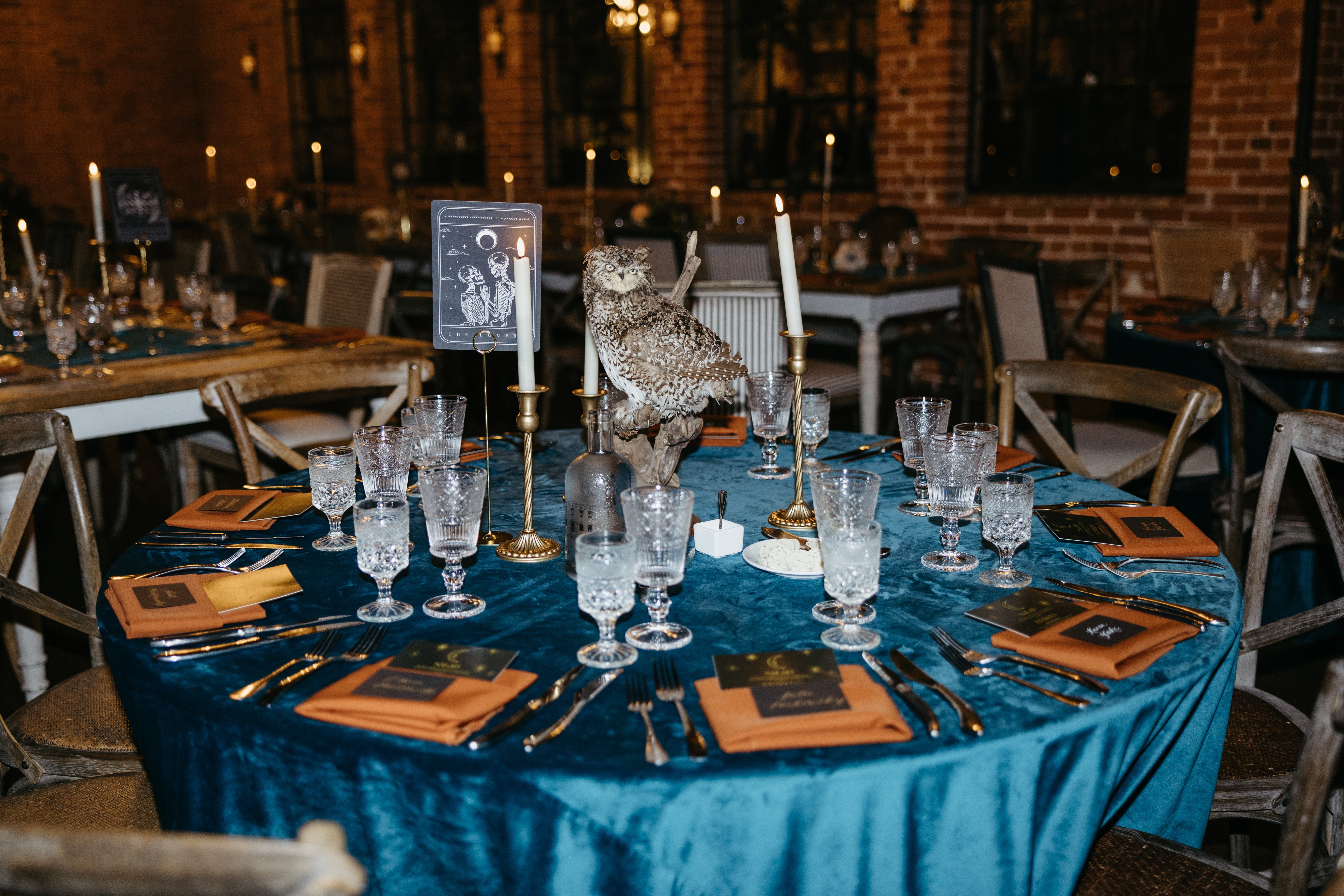 Luxury UK wedding stationery on a teal velvet-draped table with gold detailing, candles, and a dramatic owl centerpiece.
