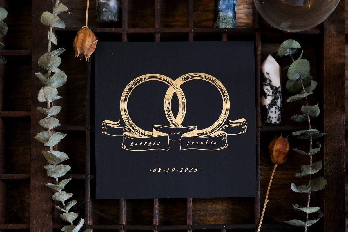 Luxury black wedding stationery featuring gold foil rings in a dramatic, gothic style, styled with dried leaves and crystals.