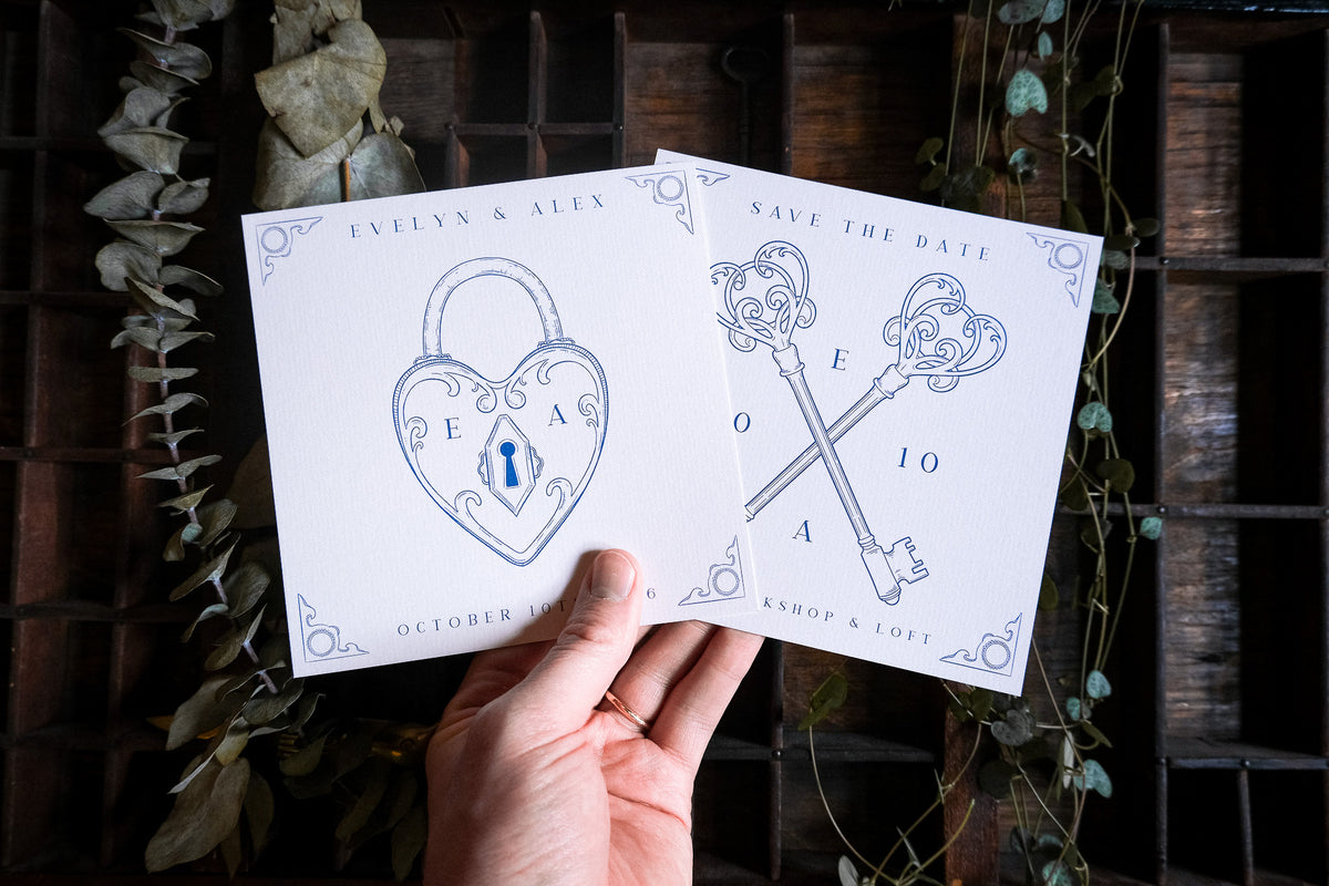 A hand displays luxury wedding stationery with a gothic heart padlock and crossed keys motif, set among dried leaves for a dramatic look.