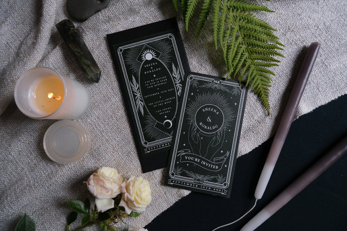 Luxury black wedding stationery in a dramatic gothic style with white details, quartz crystal, florals, and candles on textured fabric.
