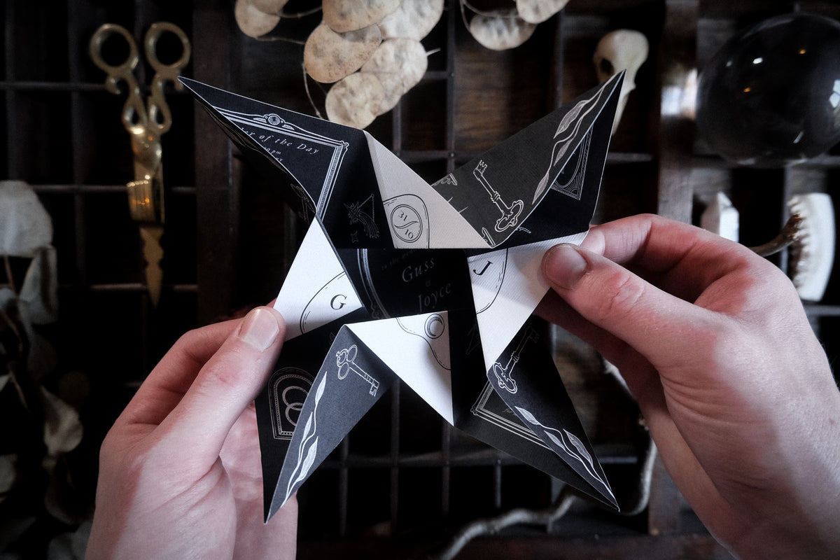 A hand folded vintage wedding invitation featuring candle and key illustrations, shown with scissors, dried leaves and trinkets.