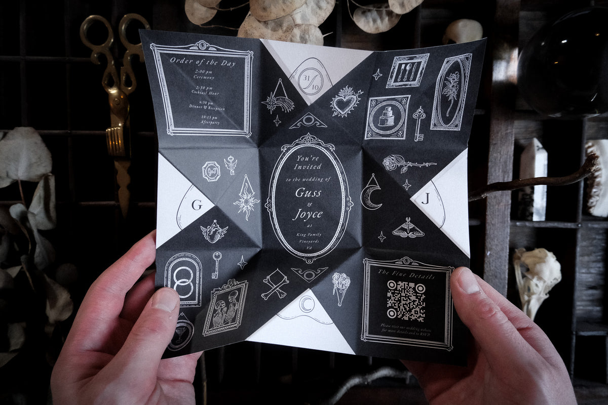 A vintage Victorian puzzle purse wedding invitation in cream and light tan, hand folded with delicate illustrations of hands holding a candle and key, displayed on a rustic wooden surface.