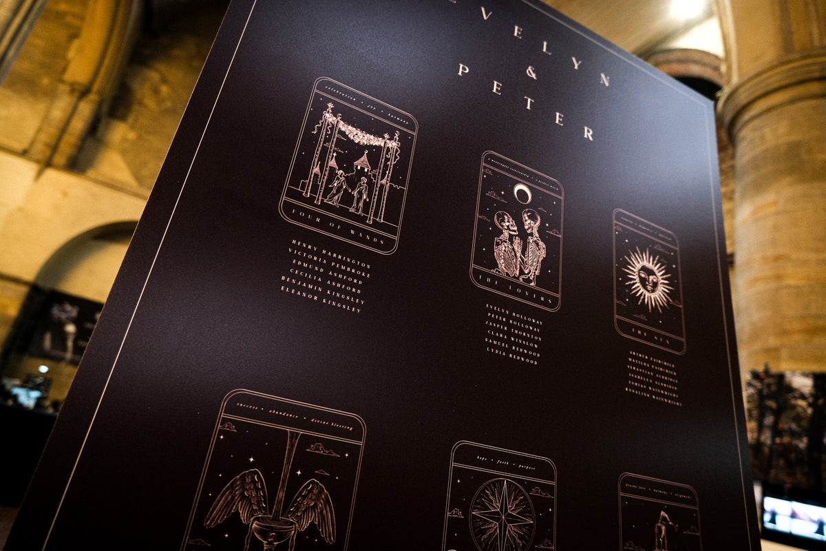 Luxury black wedding stationery display board with mystical gold foil tarot card designs, set in a dramatic gothic stone venue.