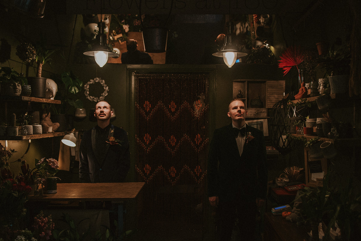 Two men in formal attire standing in a dimly lit room with decorative elements.