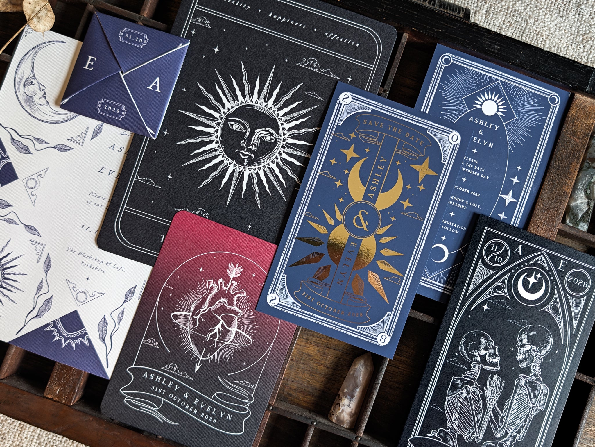 A luxury celestial wedding stationery sample pack showcasing dramatic sun, moon, and star motifs in a rich palette of black, navy, burgundy, and white. The personalised cards feature intricate details and subtle foil accents for a mystical yet romantic look. Presented neatly on a wooden tray for an elegant UK boho or alternative wedding style.