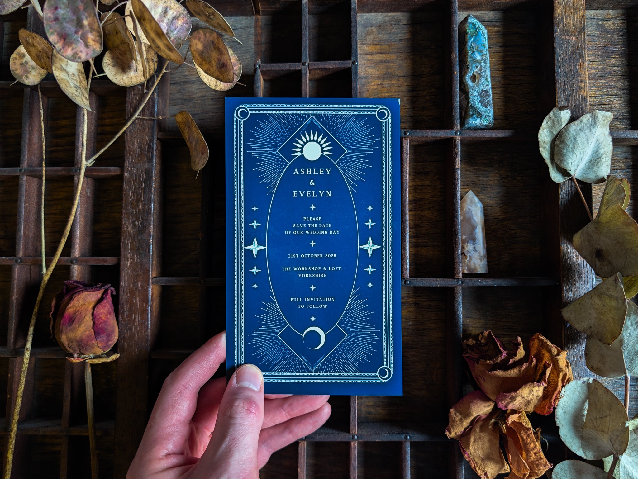 A gold foil celestial save the date card from the sample pack, held in hand.