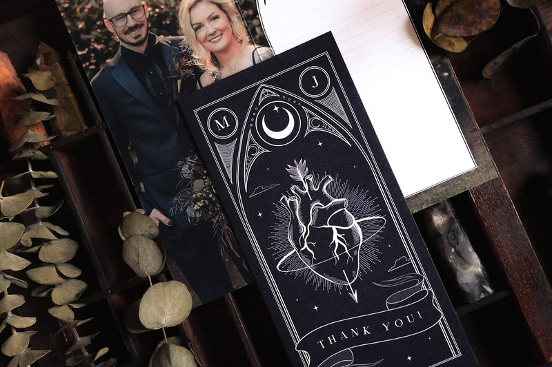 Luxury personalised wedding thank you card with a dramatic celestial heart design, shown on wood with boho dried foliage and photo.