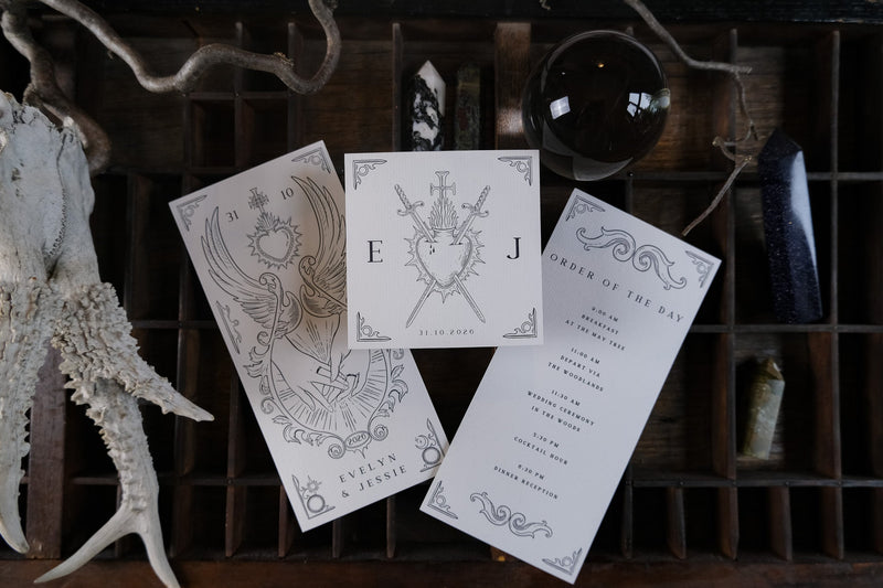 Luxury gothic wedding stationery suite with black and white invites, crystals, antlers, and a mystical dark orb on a wooden tray.