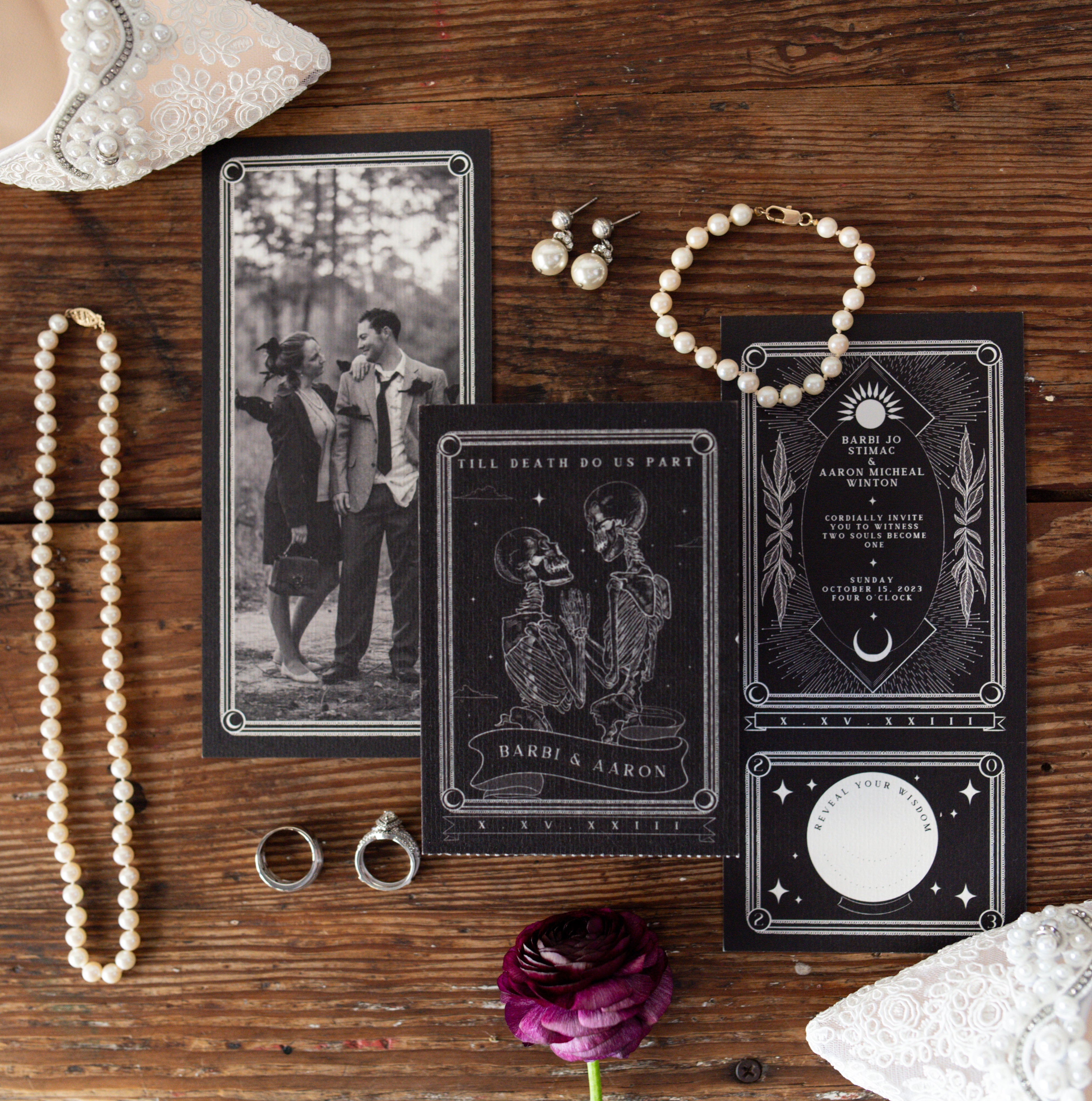 Luxury gothic wedding stationery in black with white detail, paired with pearl jewelry and vintage-inspired accessories on wood.