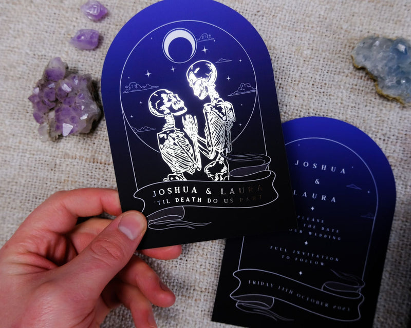 The Lovers Arched Foiled Save The Date card featuring a skeleton couple with gothic foiled accents