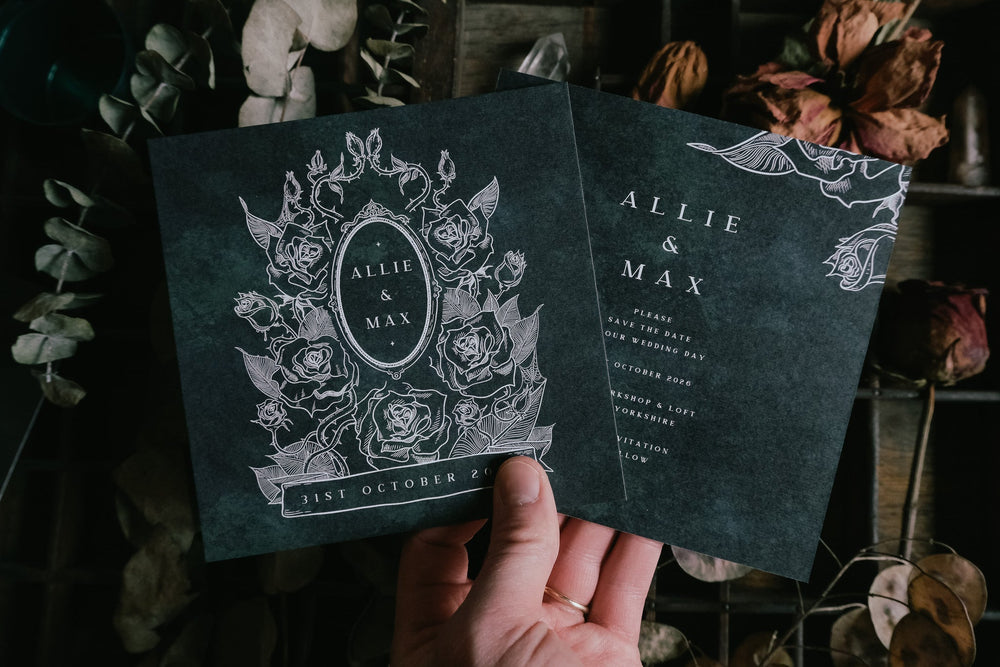 Hand holding two Thorned Rose save the dates with dark floral Victorian design