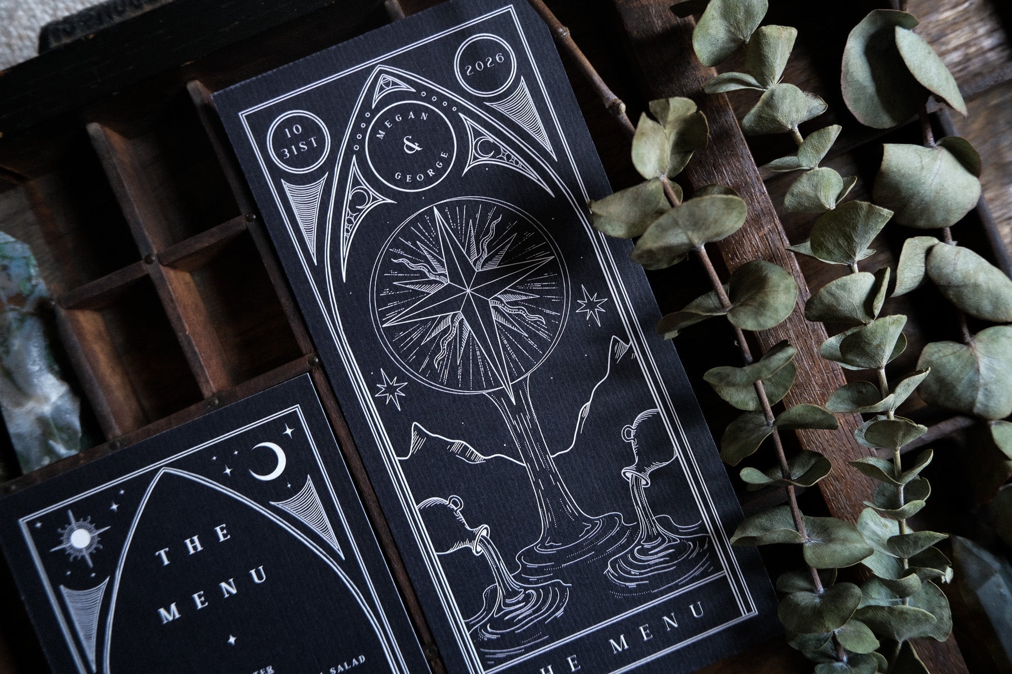 Luxury celestial wedding menu card with dramatic black and white tarot-inspired design on premium cardstock, styled with dried eucalyptus.