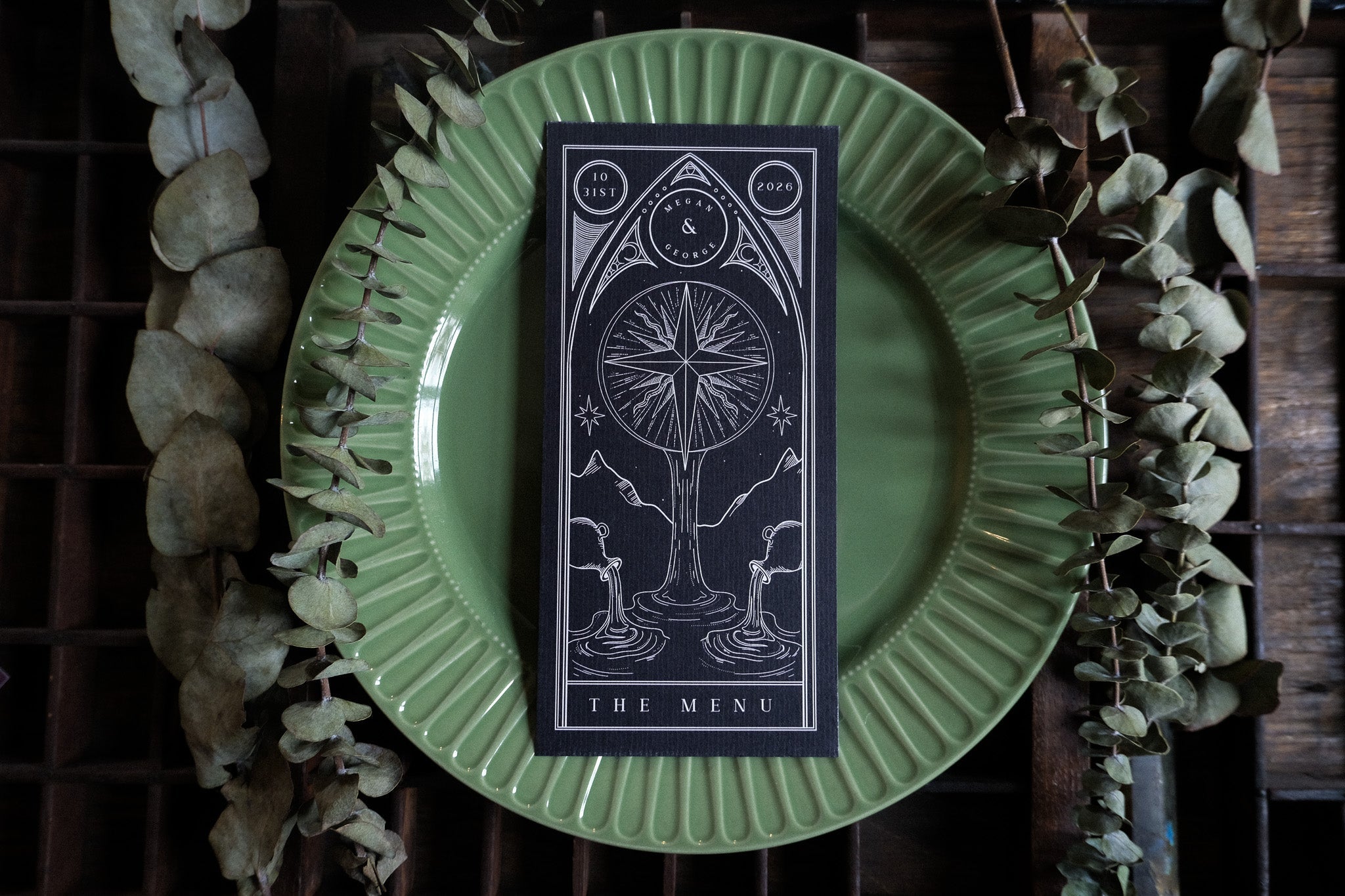 Celestial-inspired wedding menu cards with mystical black and white tarot designs on luxe paper, styled boho on rustic wood and green plate.