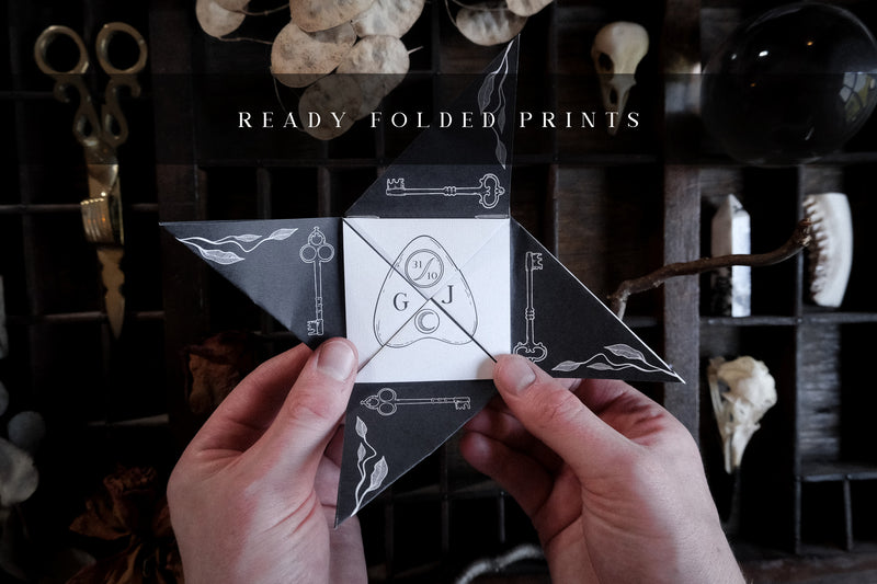A black and white star-shaped Victorian folding wedding invitation features hand illustrations, keys and wave motifs, shown amidst vintage objects.